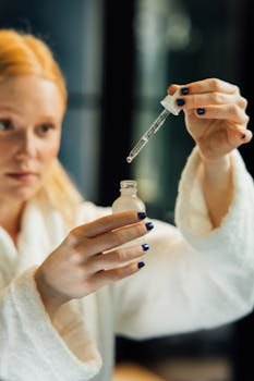 Blonde woman in a bathrobe applying serum with a dropper for skincare routine.